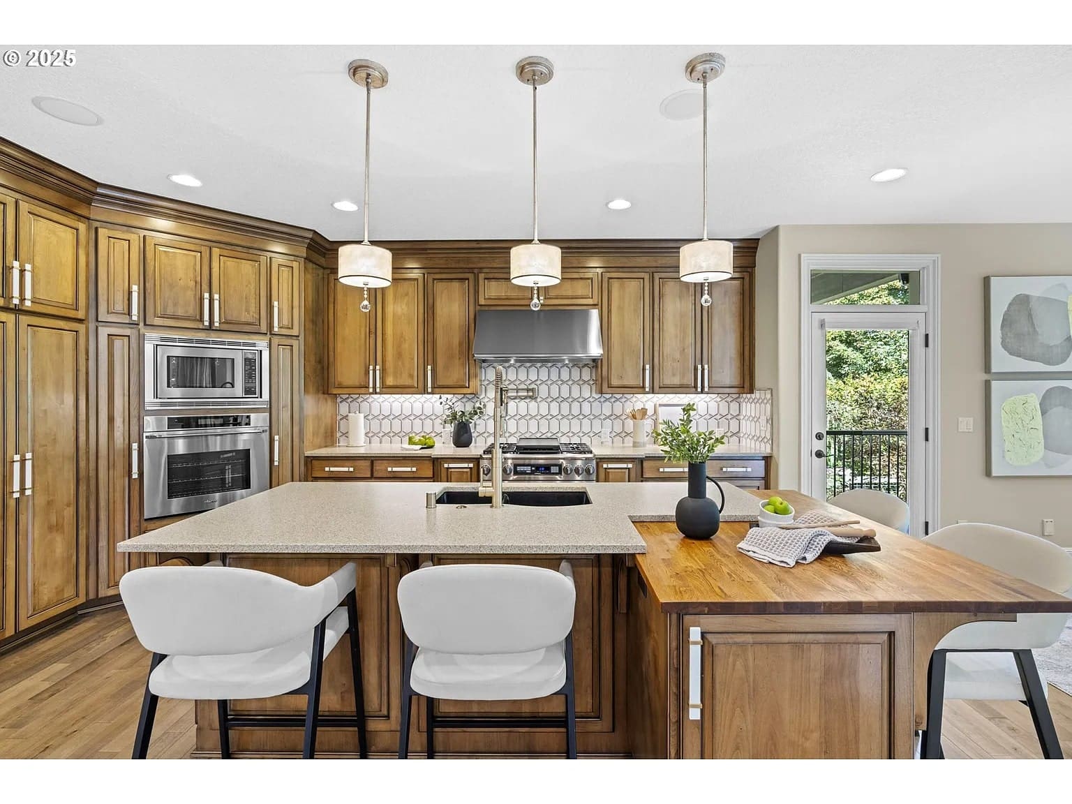 Modern kitchen with wooden cabinets, island with seating, pendant lights, and stainless steel appliances.
