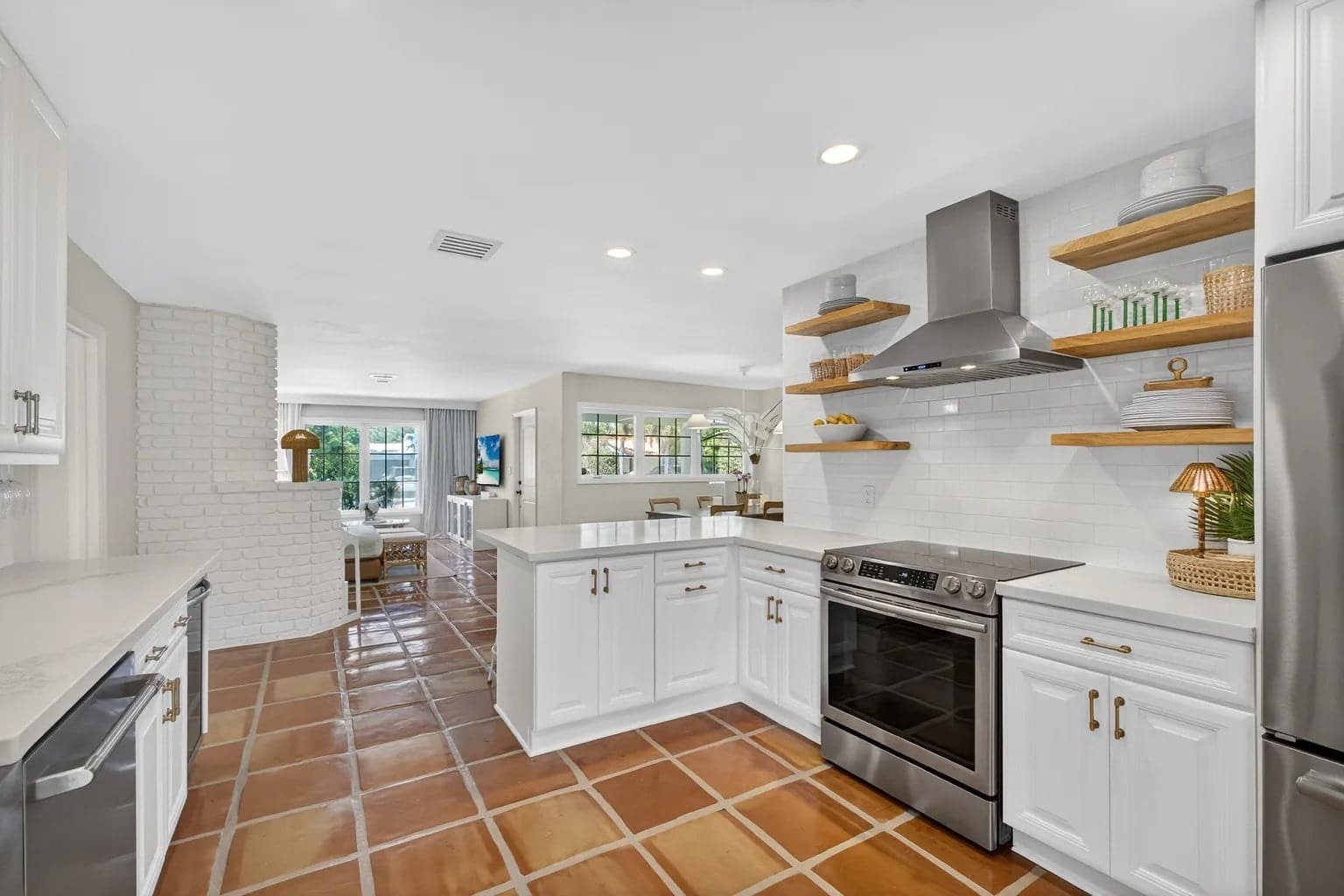 Modern kitchen with white cabinets, stainless steel appliances, open shelves, and terracotta tile flooring.
