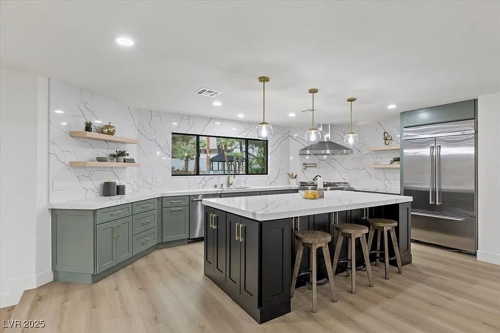 Modern kitchen with marble countertops, green cabinets, large island, and stainless steel appliances.