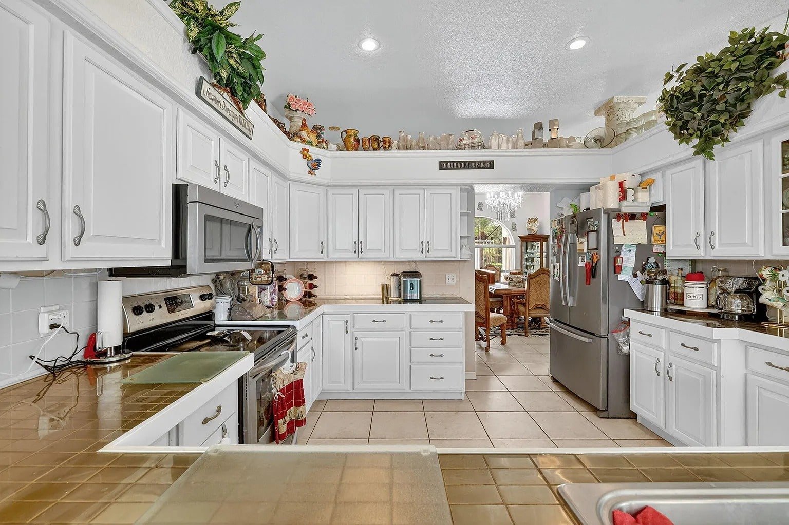 Spacious kitchen with white cabinets, stainless steel appliances, and decorative items on top shelves.