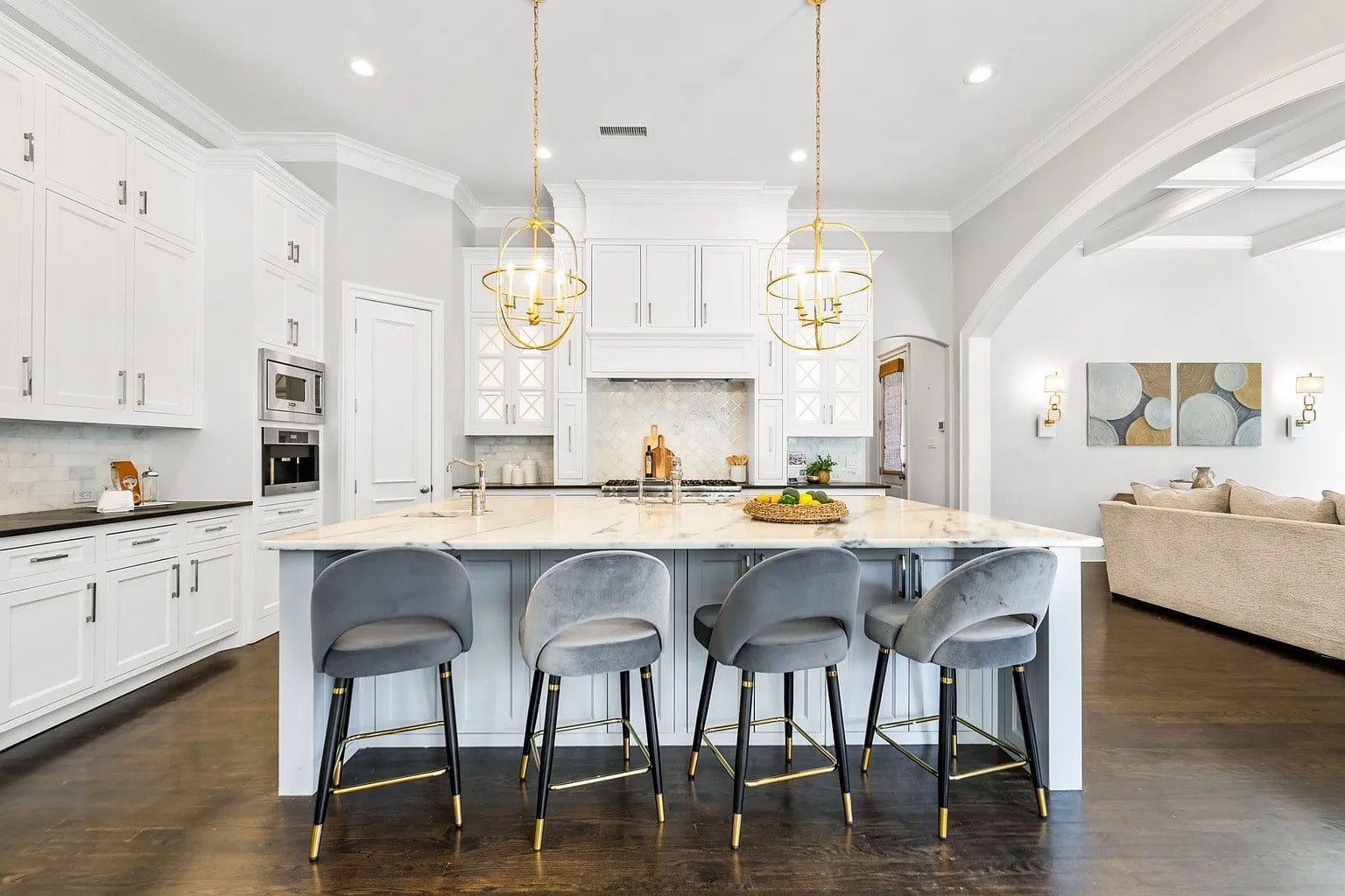 Modern kitchen with white cabinets, marble island, gray barstools, and gold pendant lights.