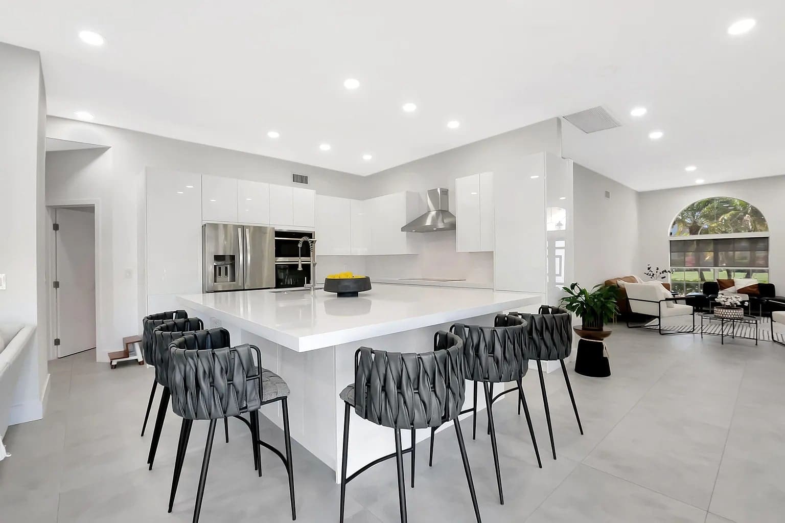 Modern kitchen with a large white island, black chairs, stainless steel appliances, and open living area.