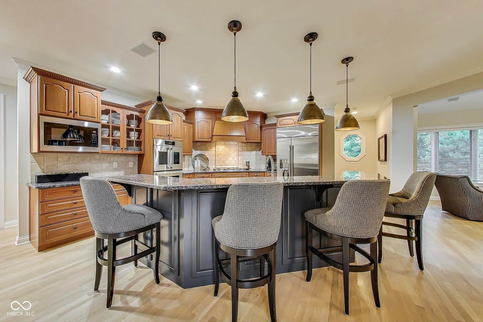 Spacious kitchen with wooden cabinets, large island, pendant lights, and upholstered bar stools.
