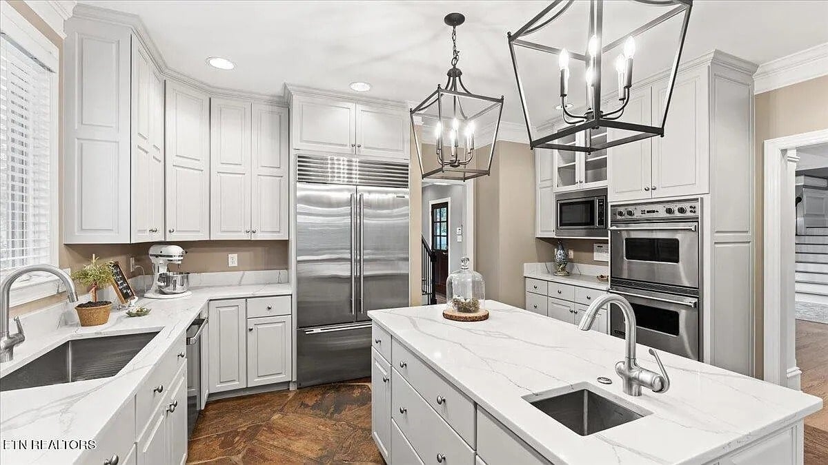 Modern kitchen with white cabinets, stainless steel appliances, and two pendant lights over an island.