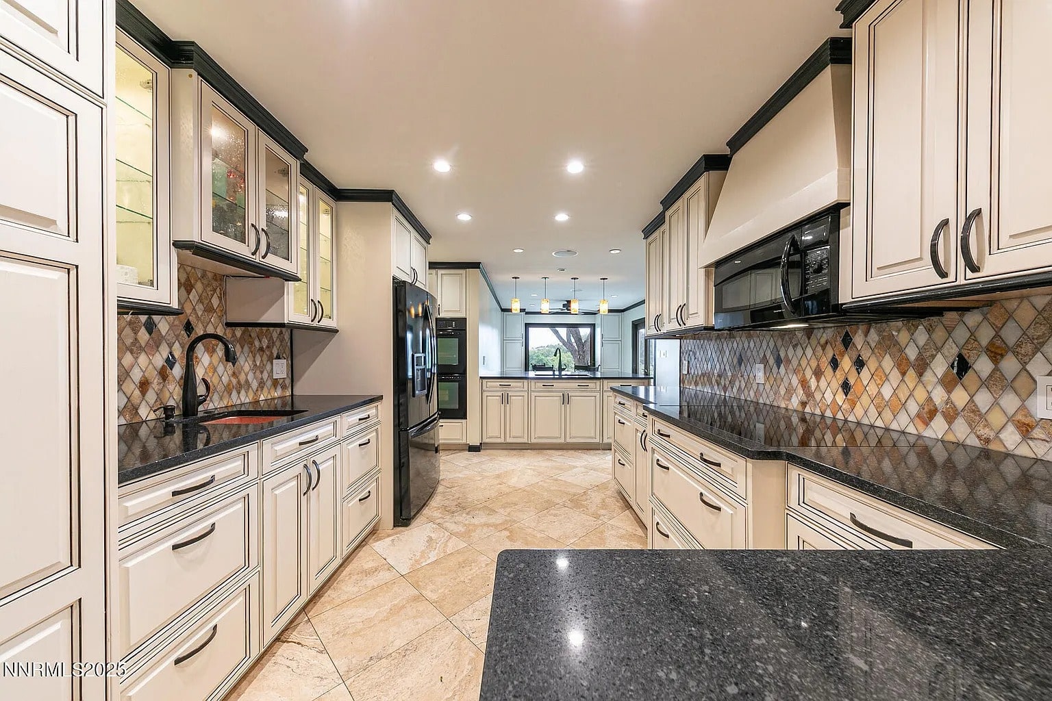Spacious kitchen with white cabinets, black countertops, and tiled backsplash, featuring modern appliances.
