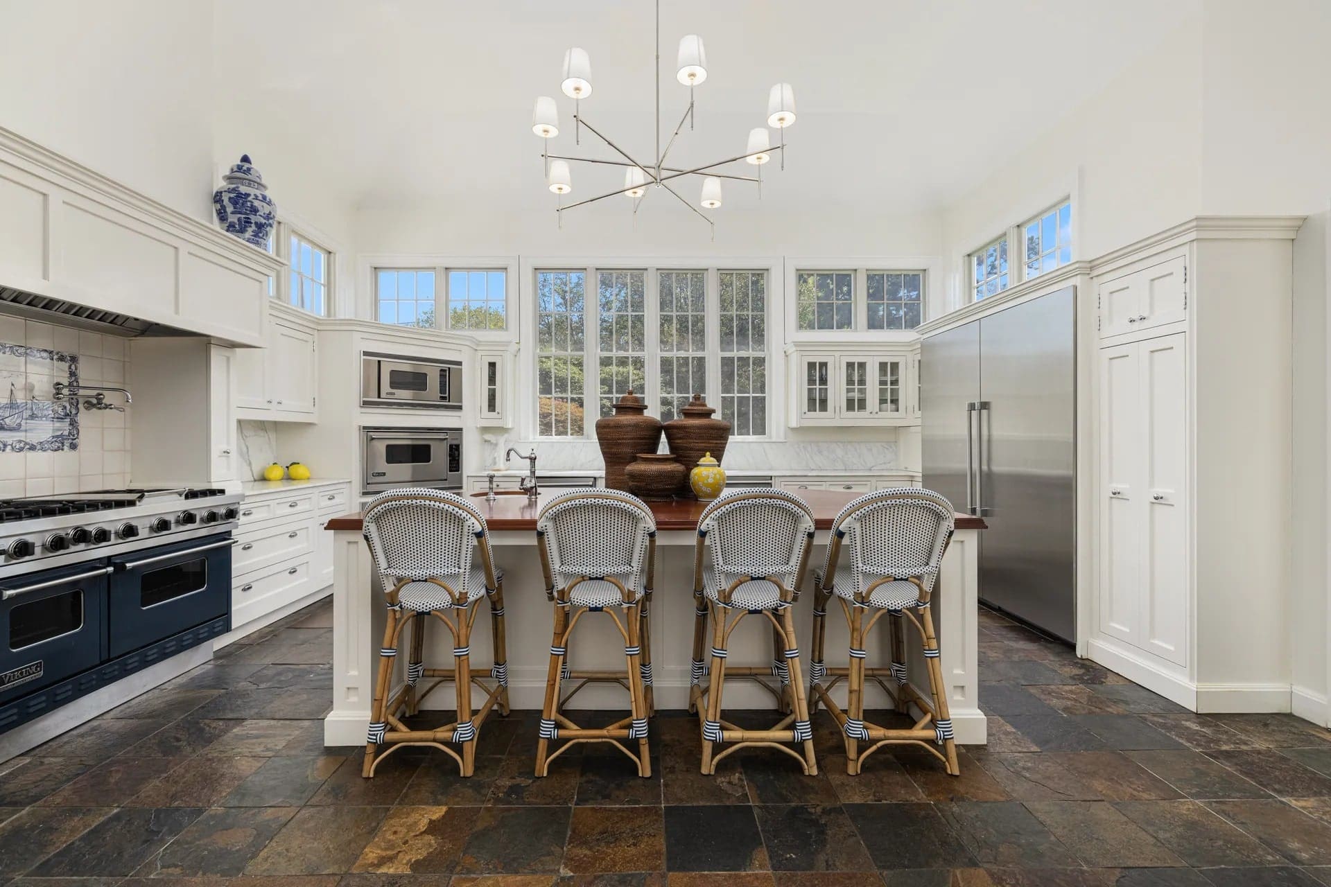 Spacious kitchen with white cabinets, large island, barstools, modern appliances, and a chandelier.