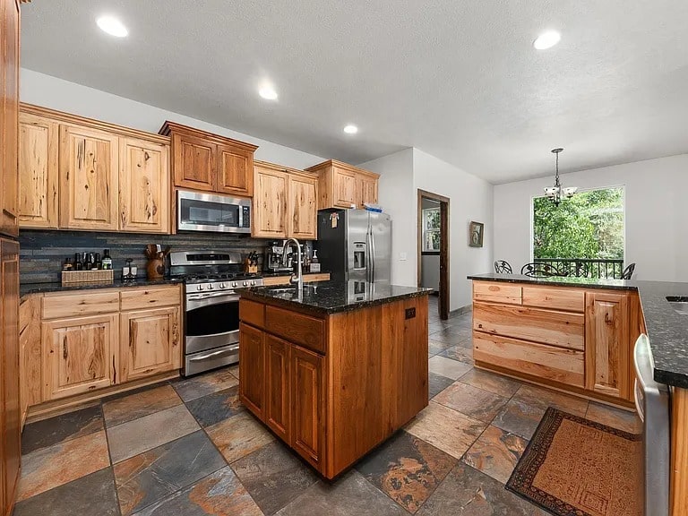 Spacious kitchen with wooden cabinets, stainless steel appliances, and a central island on tiled flooring.