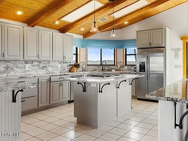 Spacious kitchen with light gray cabinets, marble countertops, and stainless steel appliances under wooden ceiling beams.