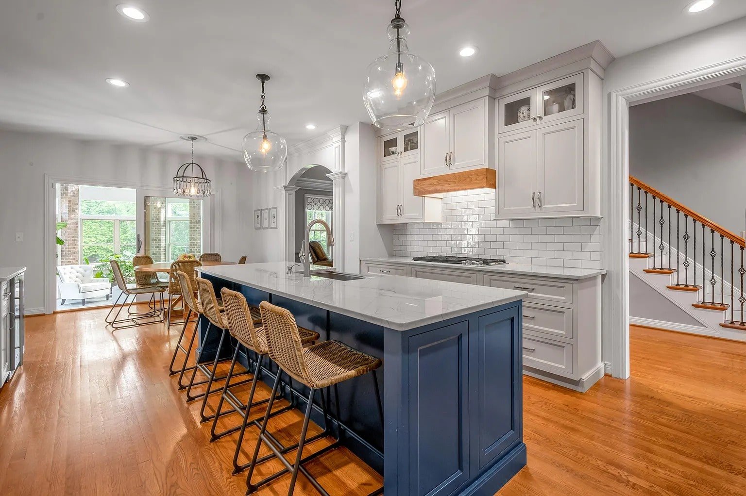 Modern kitchen with a large blue island, wicker barstools, and white cabinetry. Bright and spacious.