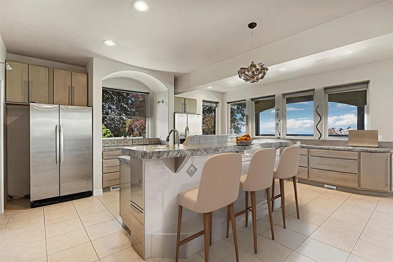 Modern kitchen with granite countertops, island seating, stainless steel appliances, and large windows with scenic views.