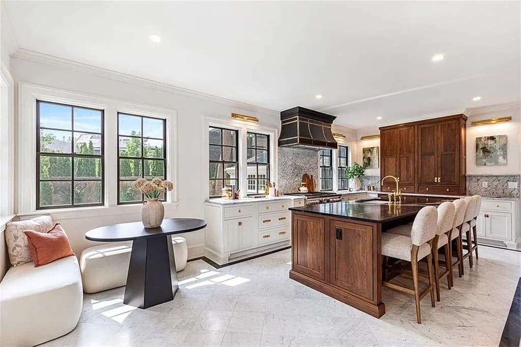 Spacious kitchen with large island, barstools, round table, and ample natural light from windows.