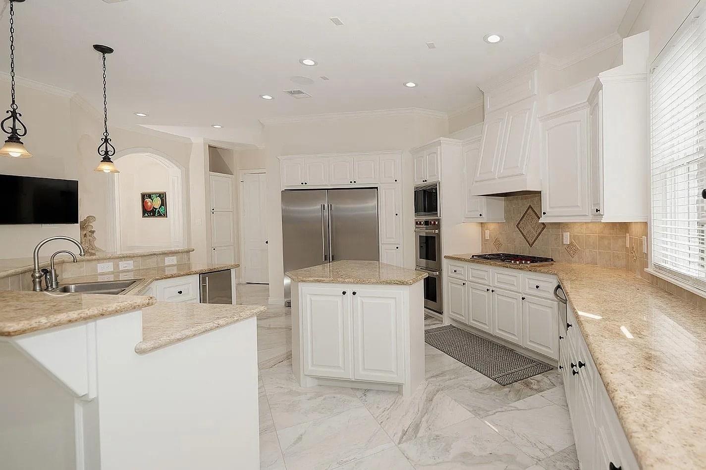 Spacious modern kitchen with white cabinets, marble floors, and stainless steel appliances.