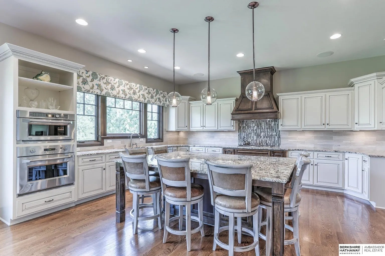 Spacious kitchen with white cabinets, large island, pendant lights, and stainless steel appliances.