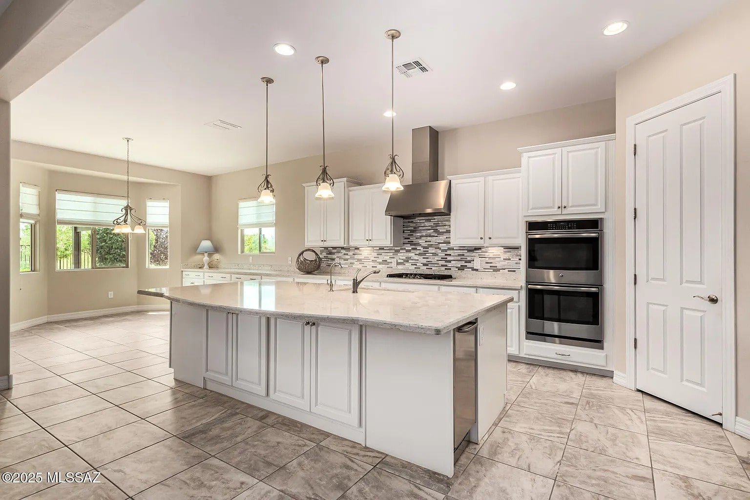 Modern kitchen with large island, pendant lights, stainless steel appliances, and white cabinetry.