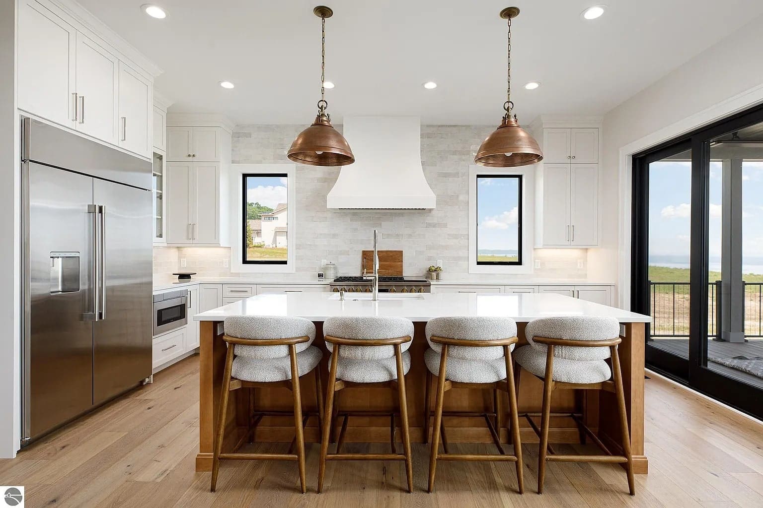 Modern kitchen with white cabinets, large island, copper pendant lights, and wooden stools.