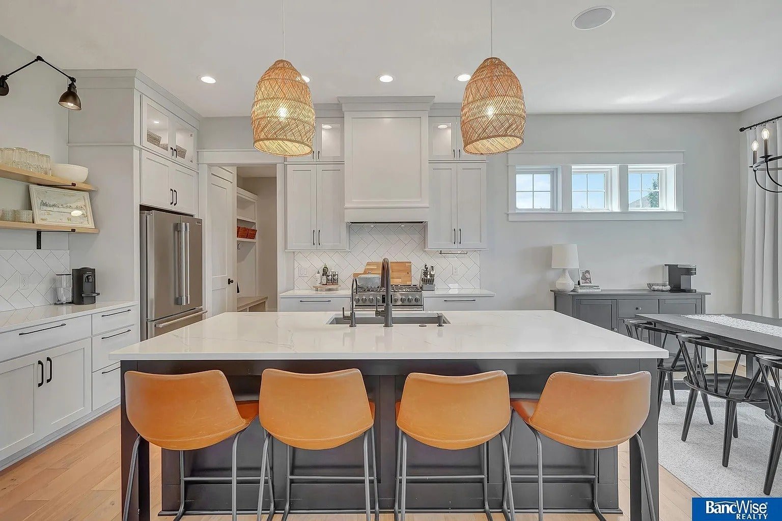 Modern kitchen with white cabinets, large island, orange barstools, and wicker pendant lights.