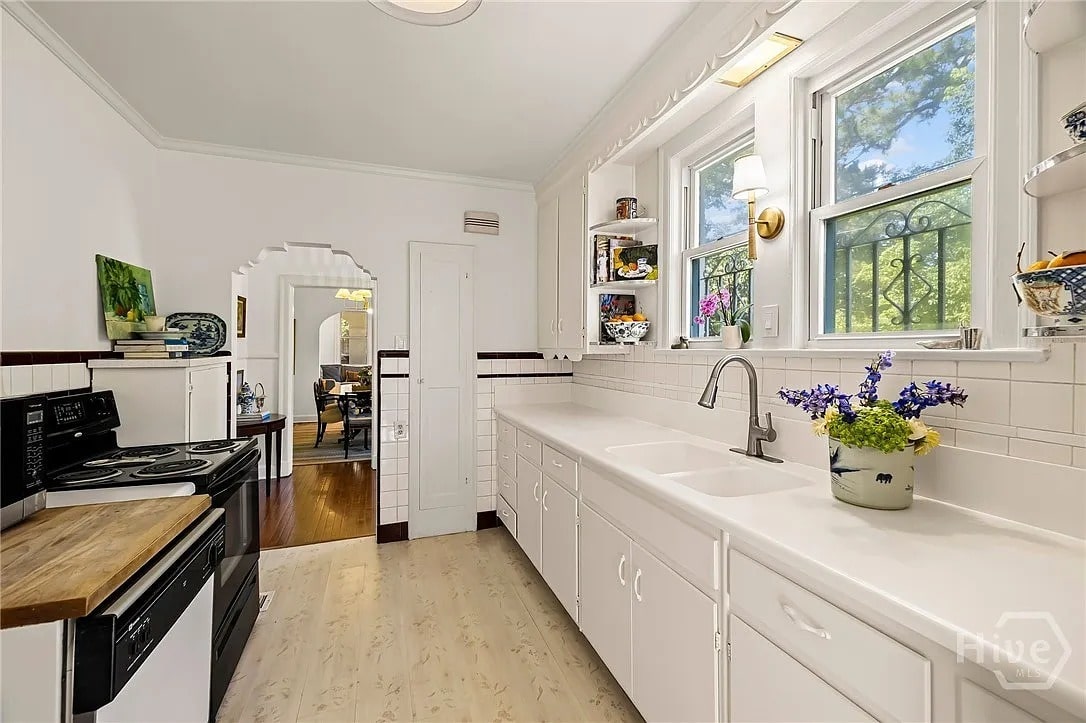 Bright kitchen with white cabinets, black stove, and window above the sink. Dining room visible.