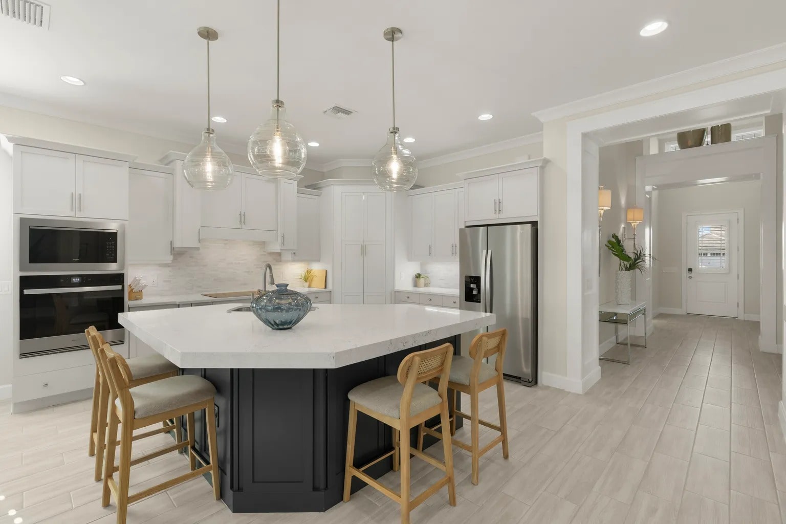 Modern kitchen with white cabinets, stainless steel appliances, large island, and pendant lighting.