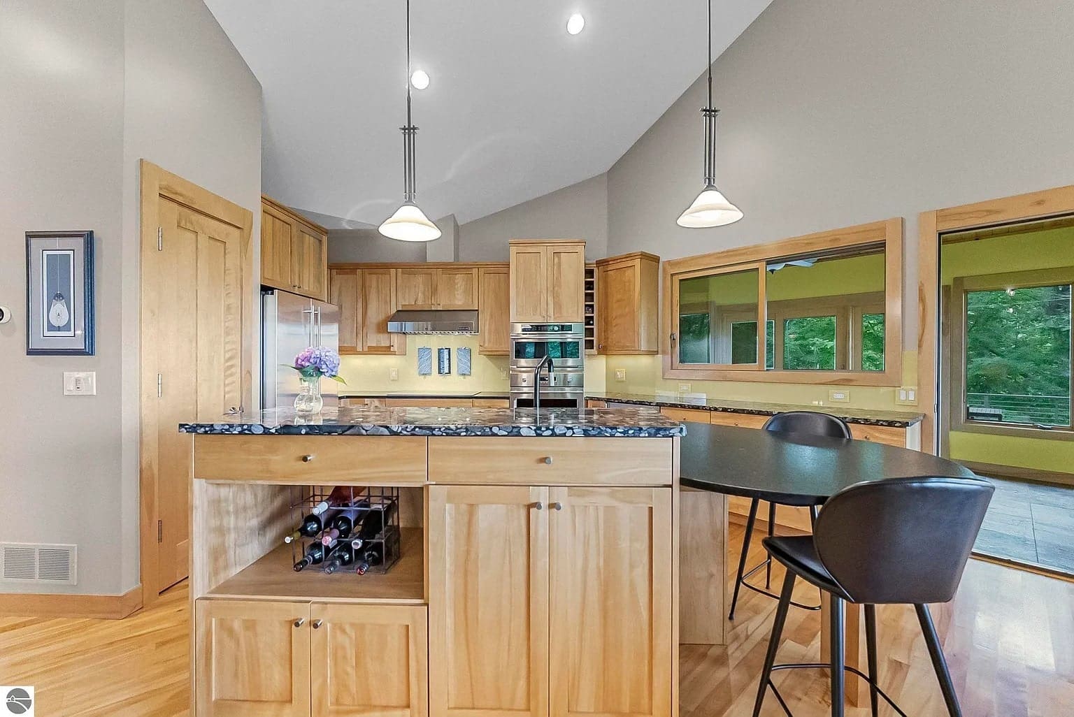 Modern kitchen with wooden cabinets, island with granite countertop, pendant lights, and bar stools.