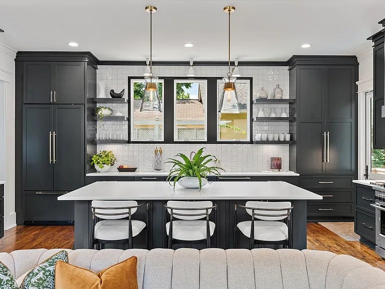 Modern kitchen with black cabinets, white countertops, pendant lights, and a central island with seating.