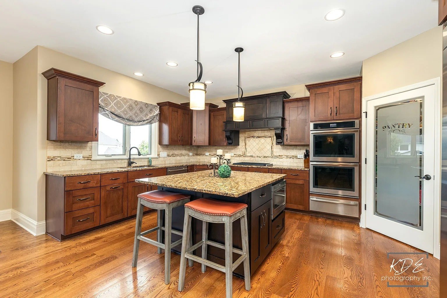 Spacious kitchen with wooden cabinets, granite island, double oven, and pantry door.