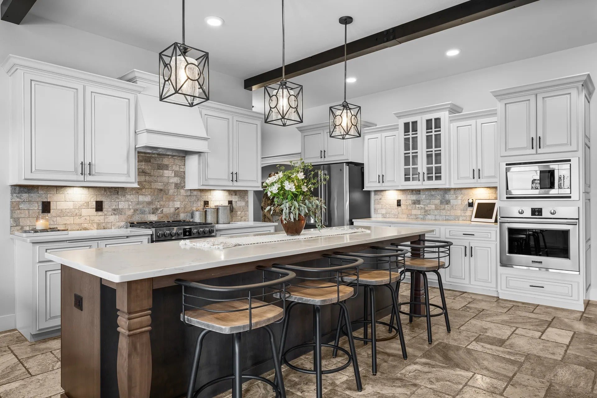 Modern kitchen with white cabinets, large island, barstools, pendant lights, and stainless steel appliances.