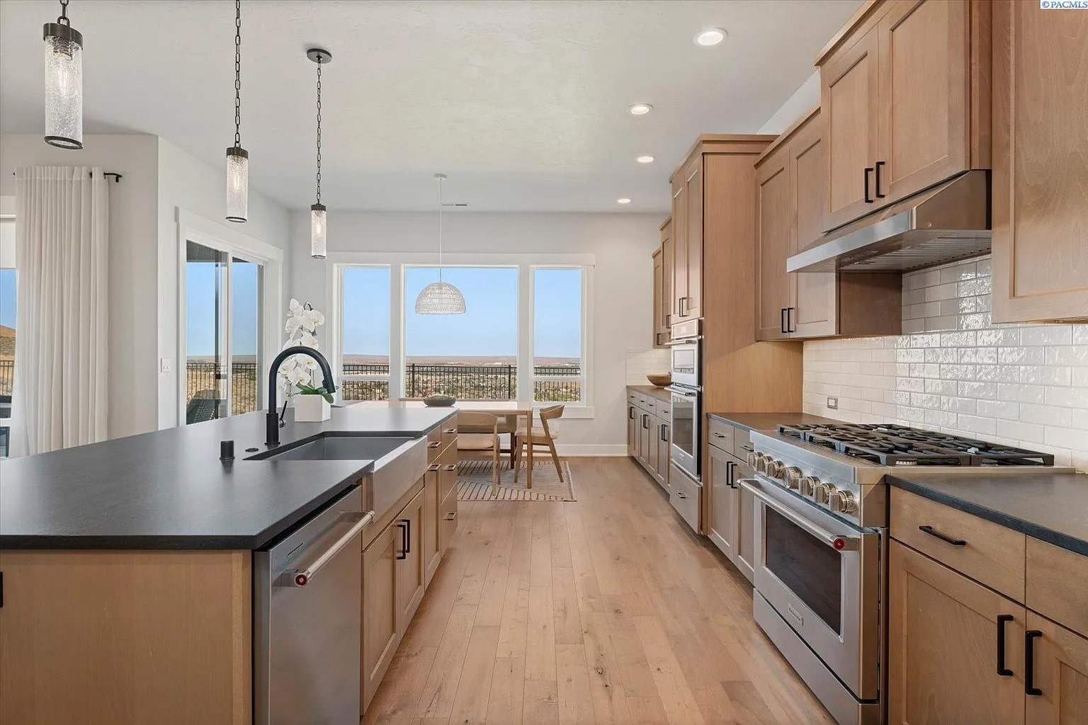Modern kitchen with wooden cabinets, black countertops, stainless steel appliances, and large windows with a view.