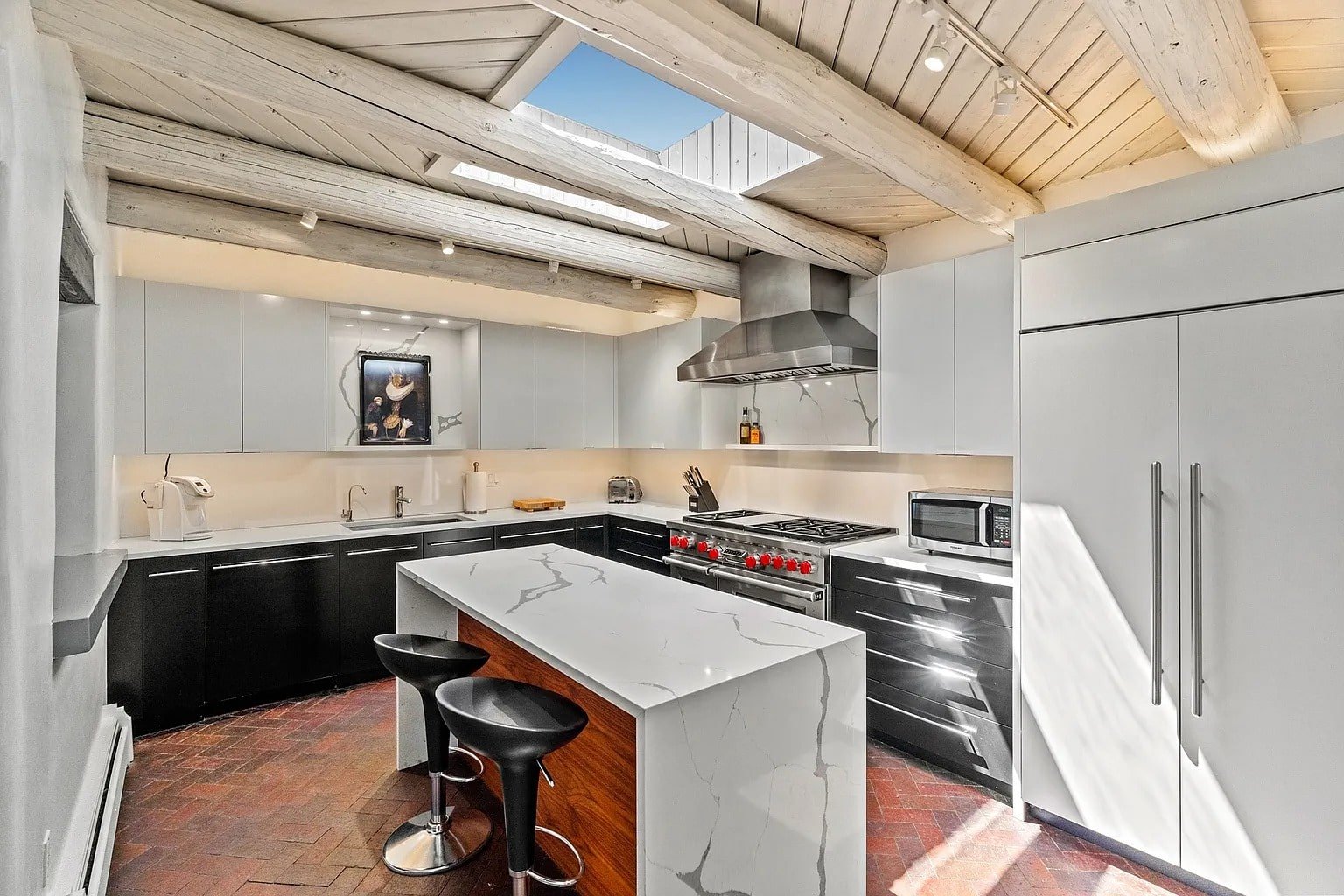 Modern kitchen with skylight, marble island, black and white cabinets, and stainless steel appliances.
