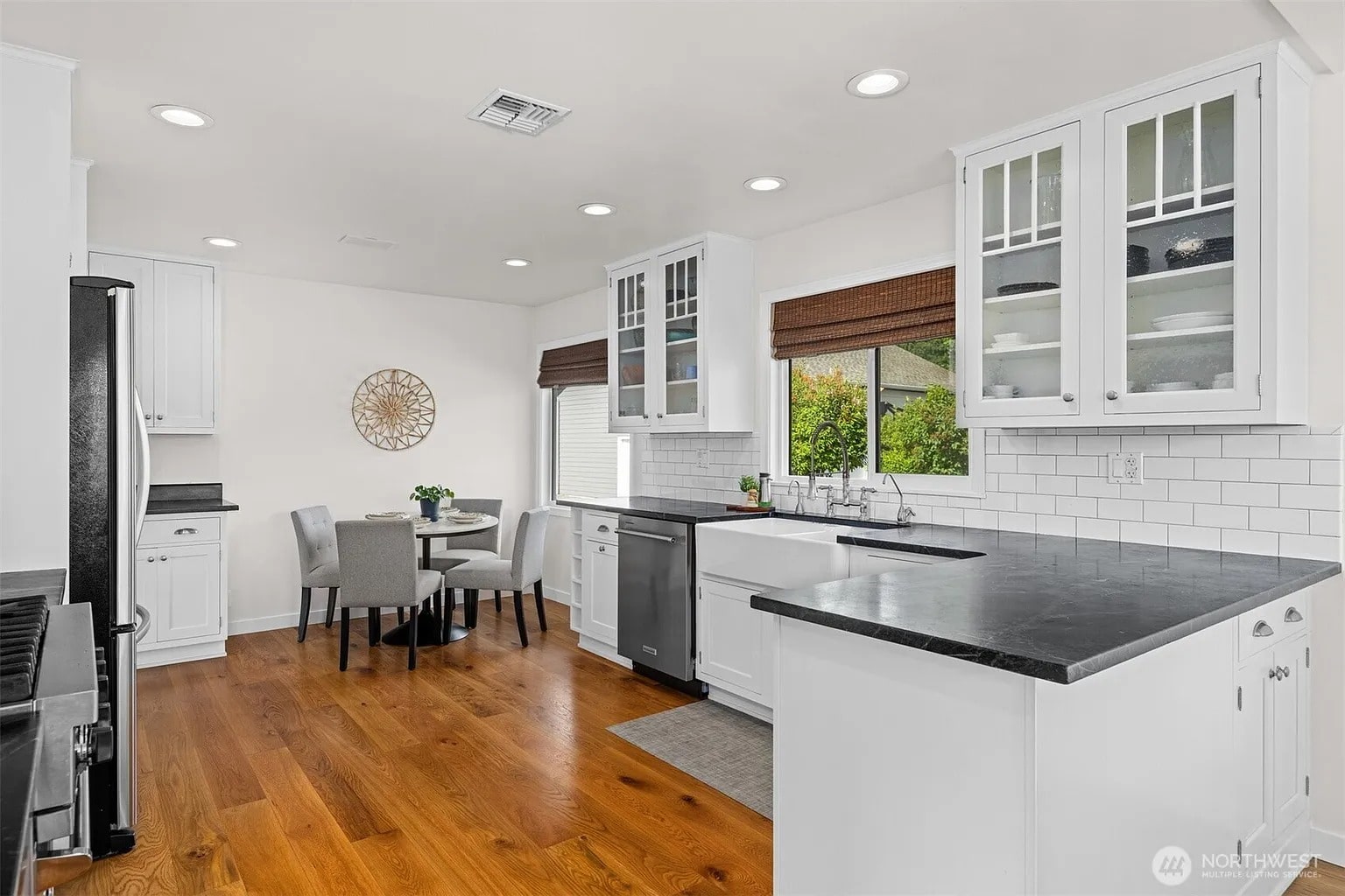 Modern kitchen with white cabinets, black countertops, hardwood floors, and a small dining area with gray chairs.