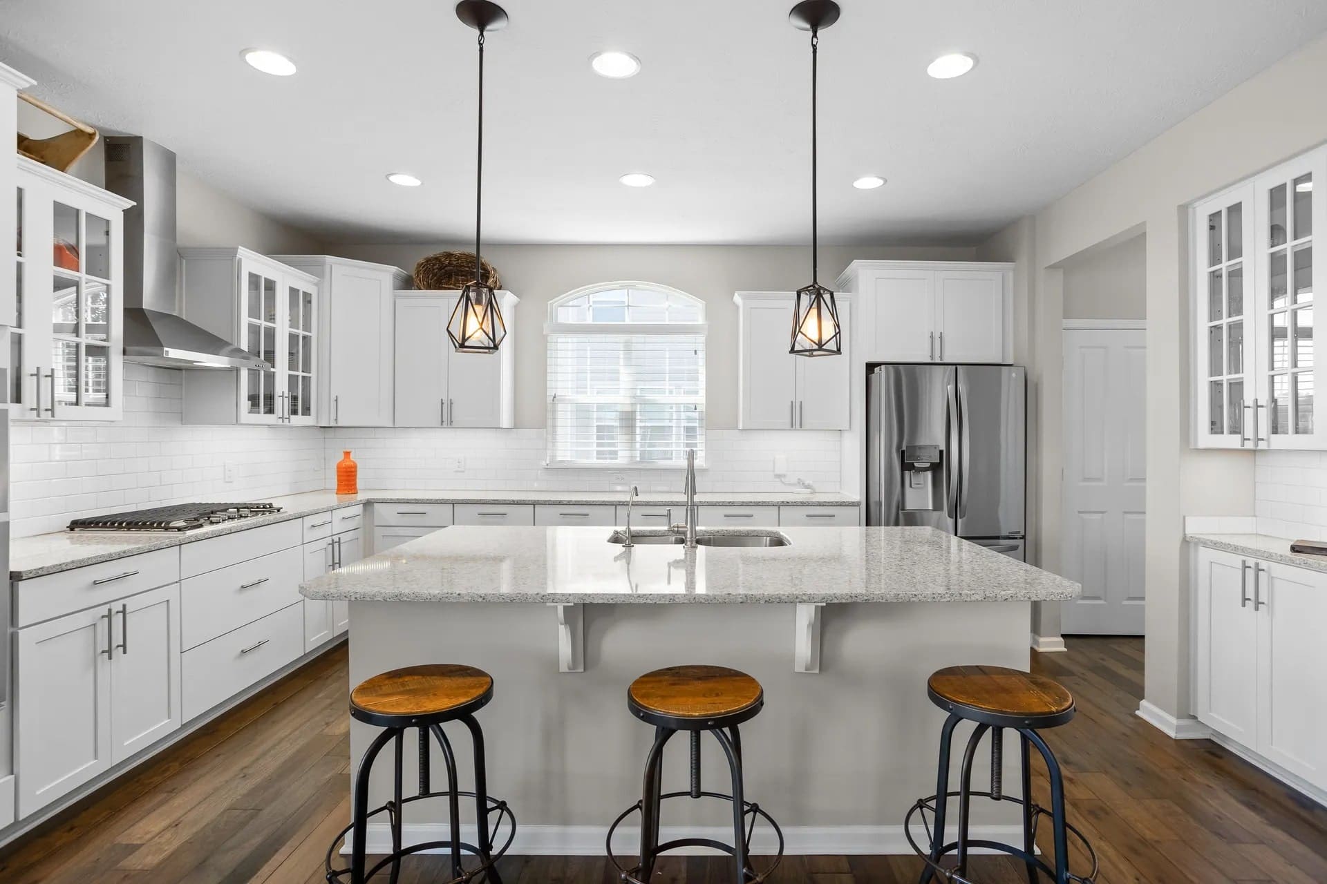 Modern kitchen with white cabinets, granite island, three stools, pendant lights, and stainless steel appliances.