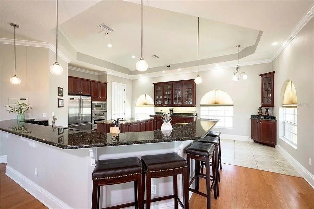 Spacious kitchen with dark wood cabinets, granite countertops, and bar stools under pendant lights.