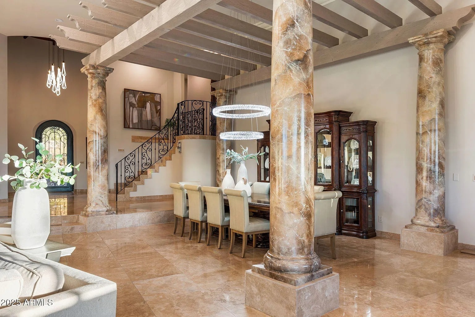 Elegant dining room with marble columns, chandelier, and a large dining table with upholstered chairs.