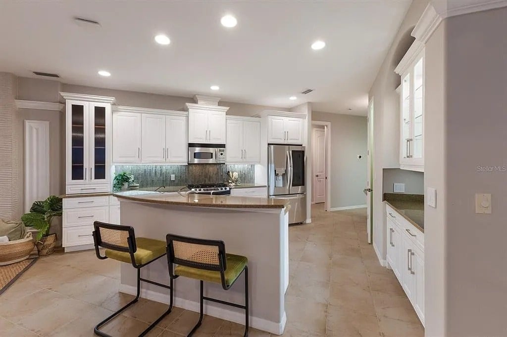 Modern kitchen with white cabinets, stainless steel appliances, and two bar stools at a counter.