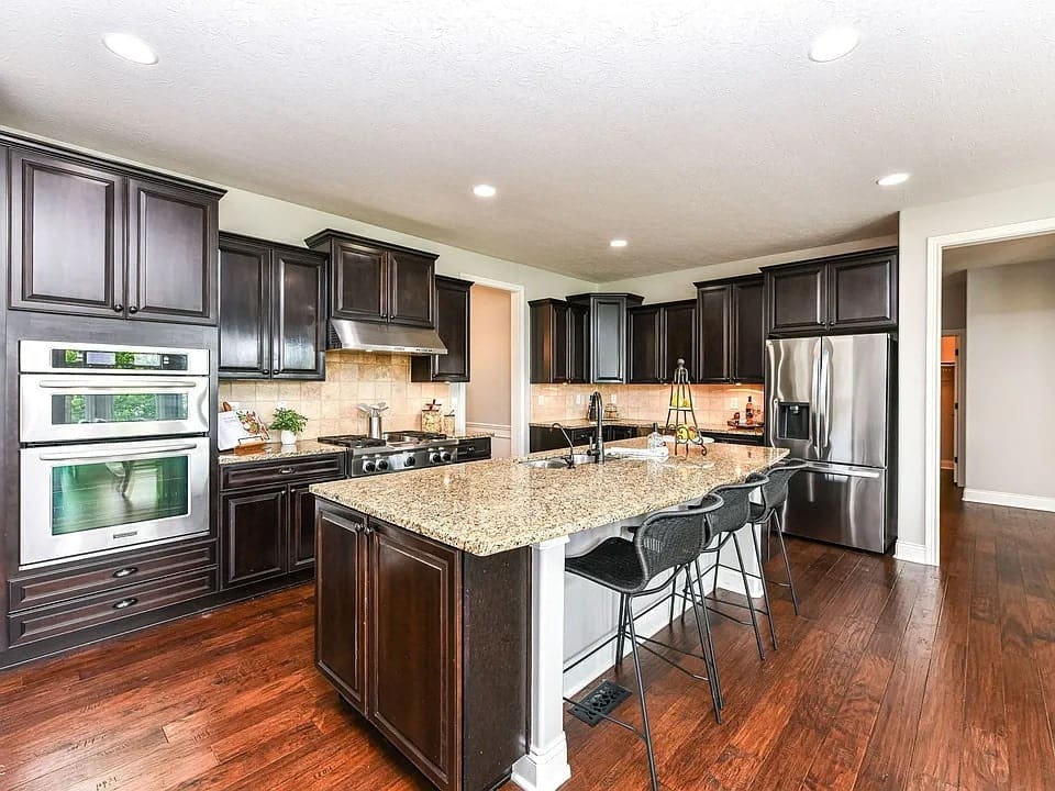 Modern kitchen with dark wood cabinets, granite countertops, stainless steel appliances, and a central island with stools.