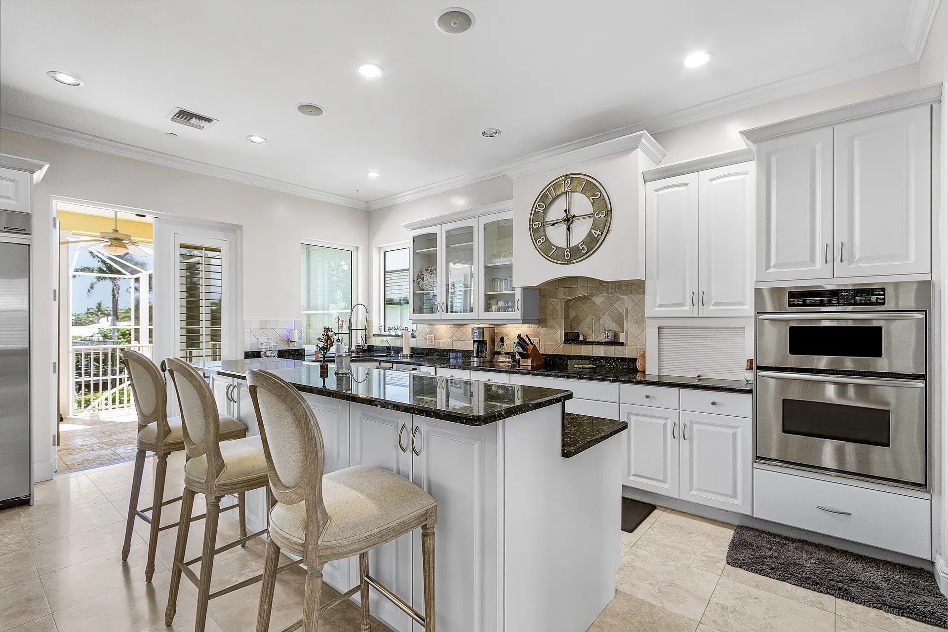 Modern kitchen with white cabinets, black countertops, bar stools, and stainless steel appliances.