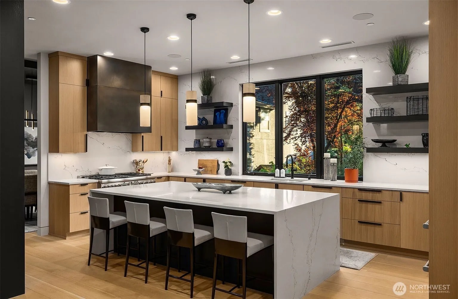 Modern kitchen with large island, pendant lights, wooden cabinets, and a window with outdoor view.