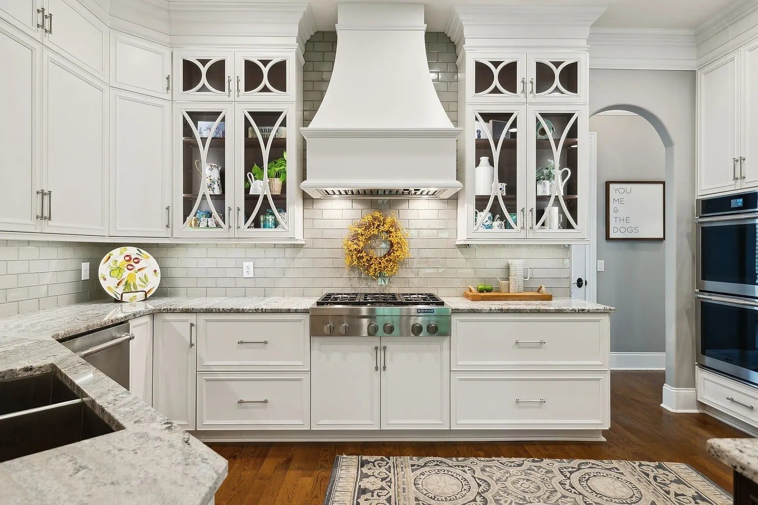 Modern kitchen with white cabinets, stainless steel appliances, decorative backsplash, and a central wreath.