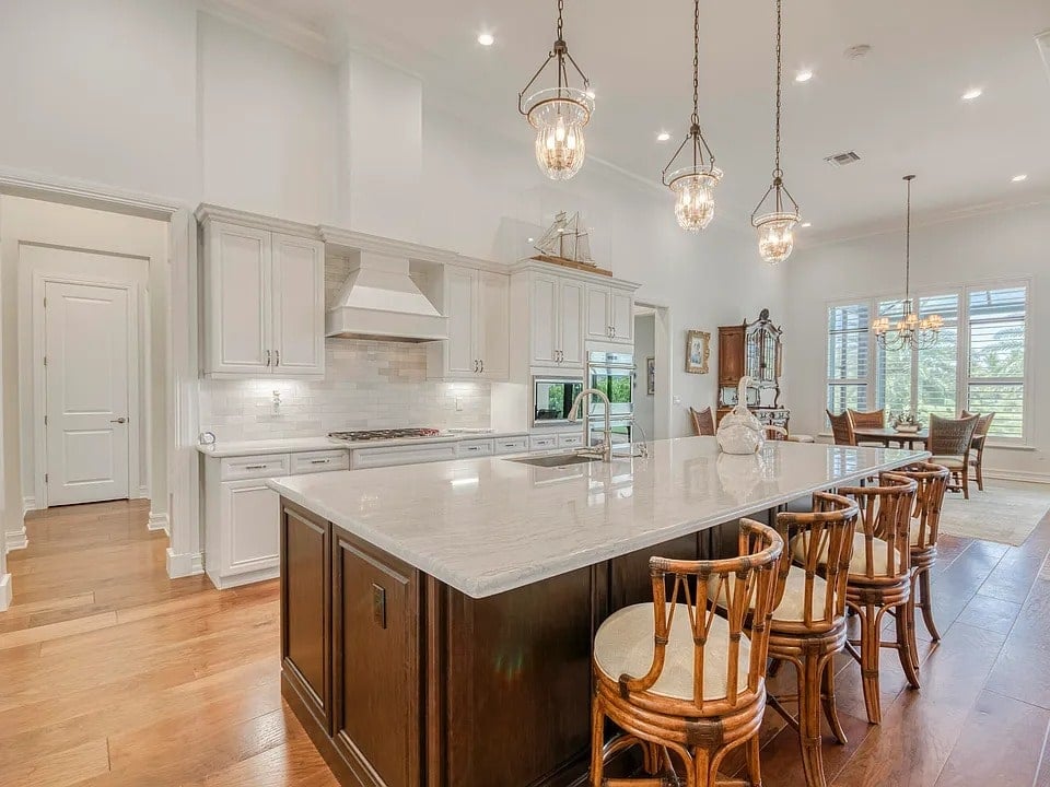 Spacious kitchen with a large island, wooden chairs, pendant lights, and a dining area in the background.