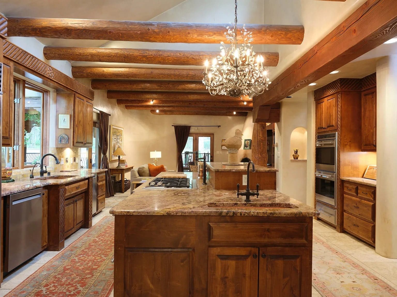 Rustic kitchen with wooden beams, chandelier, large island, and modern appliances. Cozy seating area visible.