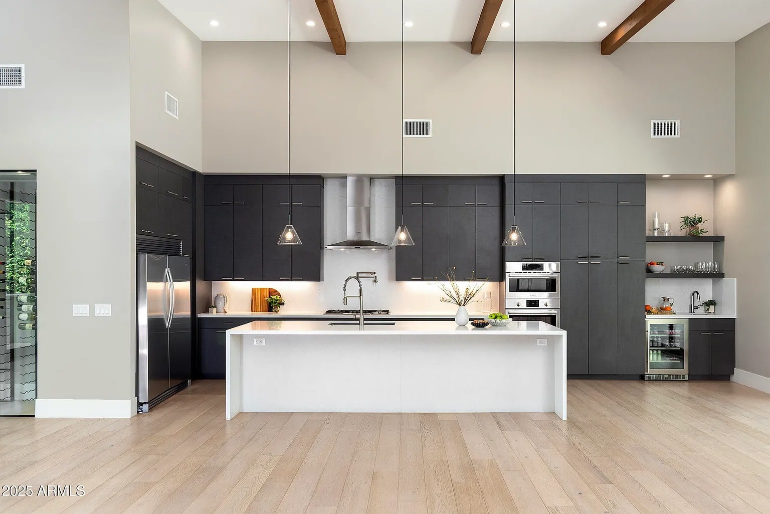 Modern kitchen with dark cabinets, white island, stainless steel appliances, and pendant lighting.