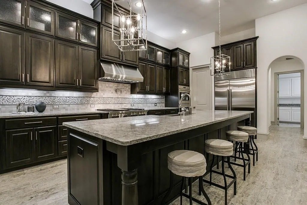 Modern kitchen with dark wood cabinets, large island, stainless steel appliances, and pendant lighting.