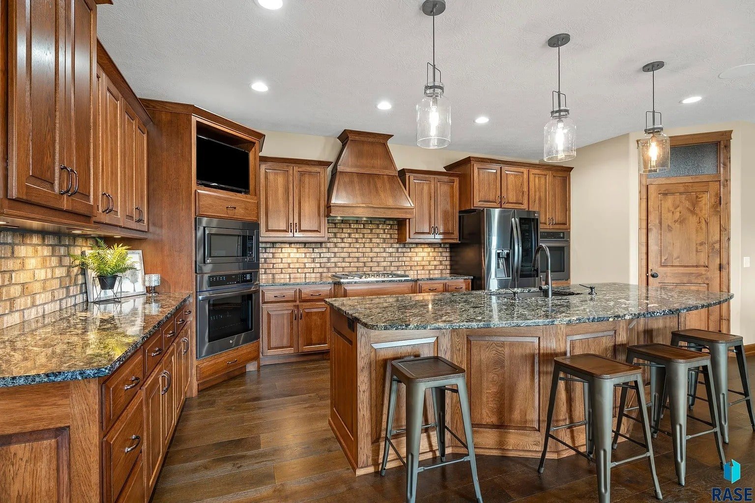 Spacious kitchen with wooden cabinets, brick backsplash, granite countertops, and a central island with stools.