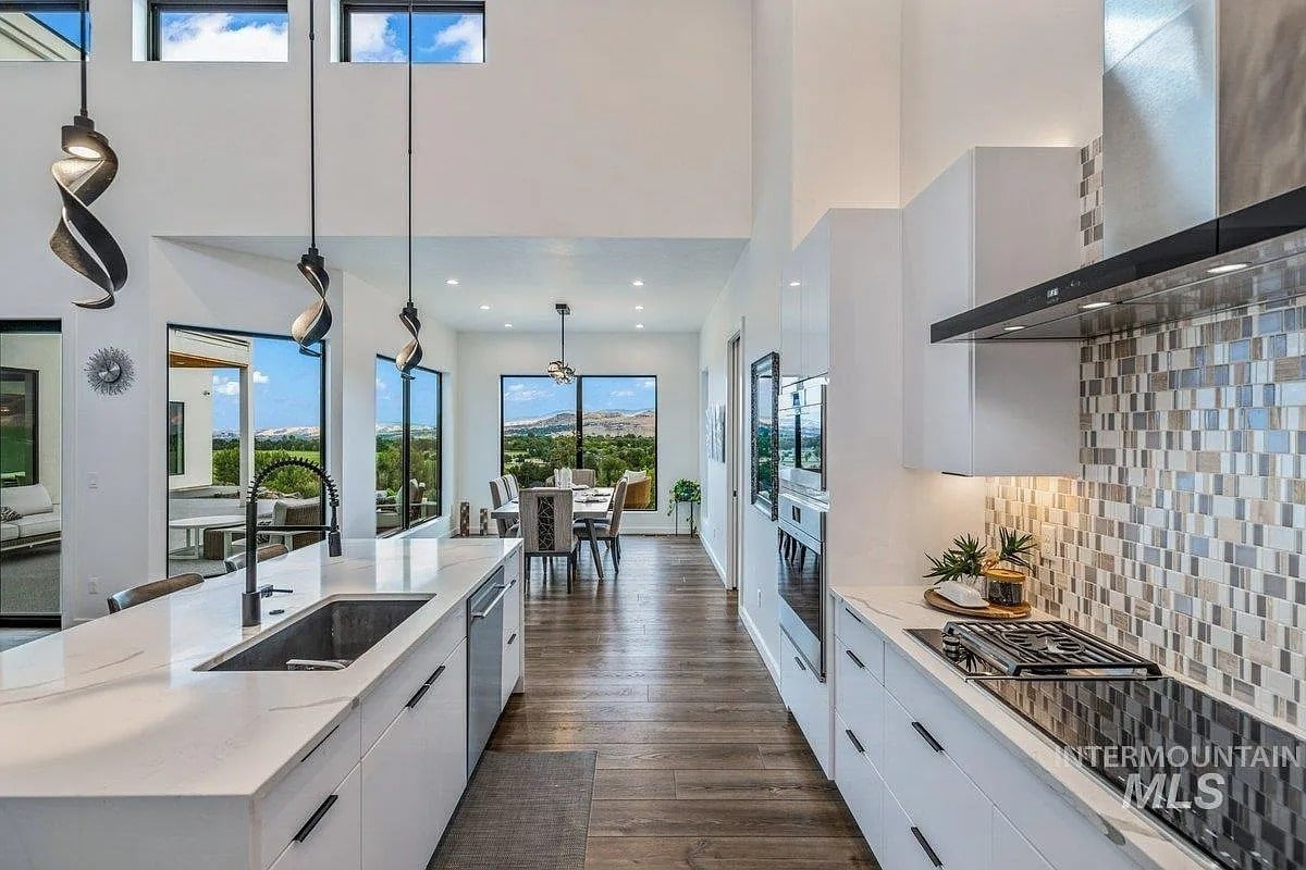 Modern kitchen and dining area with white cabinets, large windows, and scenic outdoor view.