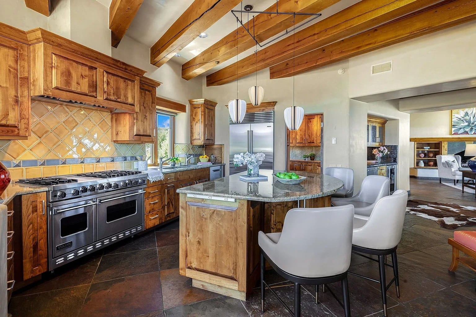 Spacious kitchen with wooden cabinets, island with seating, stainless steel appliances, and exposed beams.