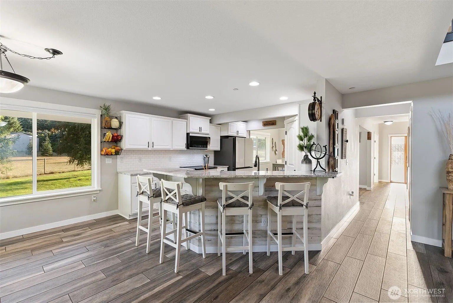 Modern kitchen with white cabinets, large island with barstools, and wood flooring. Bright window view.