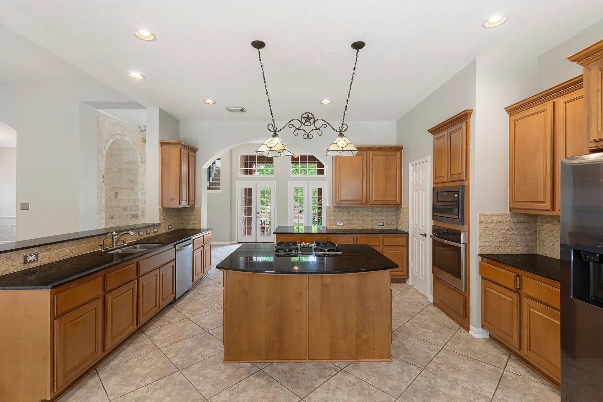 Spacious kitchen with wooden cabinets, black countertops, central island, and large windows.