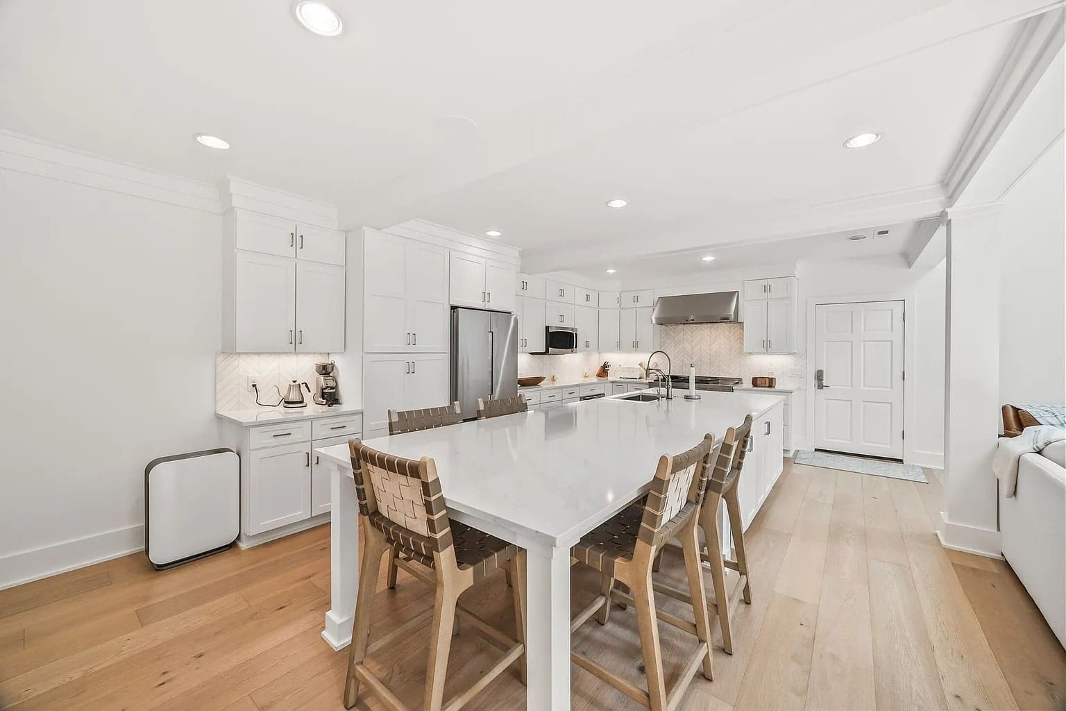 Modern kitchen with white cabinets, large island, bar stools, stainless steel appliances, and wood flooring.