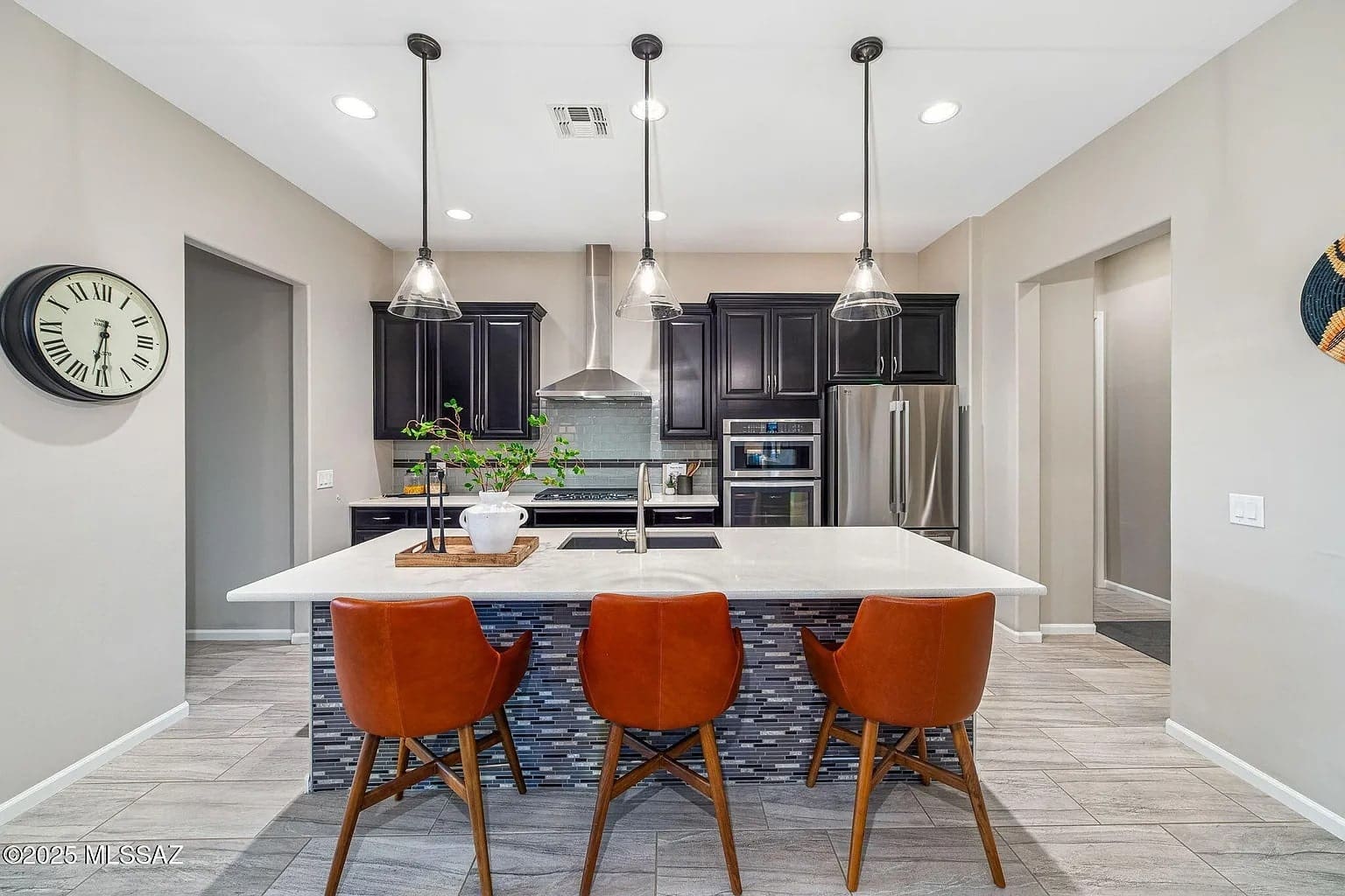 Modern kitchen with dark cabinets, stainless steel appliances, and three orange chairs at a central island.