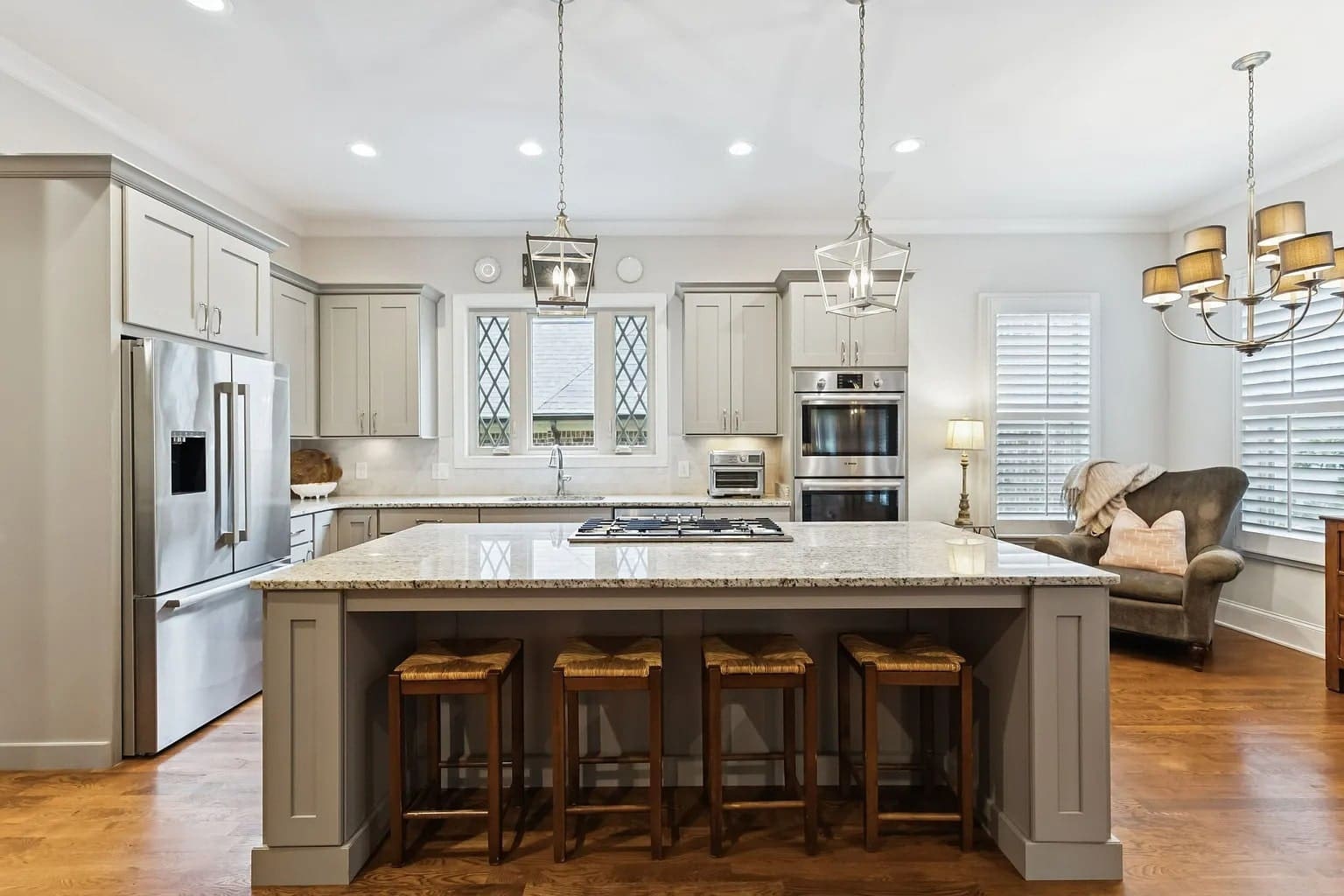 Modern kitchen with a large island, bar stools, stainless steel appliances, and elegant lighting fixtures.
