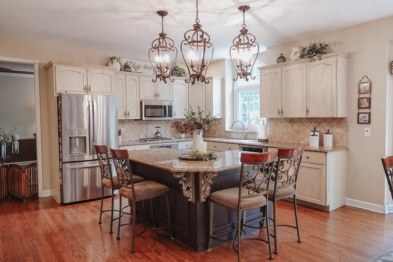 Elegant kitchen with wooden cabinets, island with ornate chairs, and three decorative pendant lights.